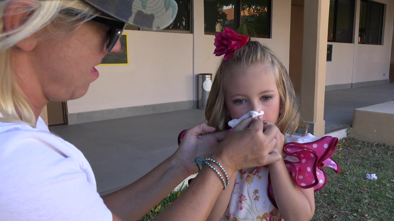 Woman wiping a young girl's nose outside a building.