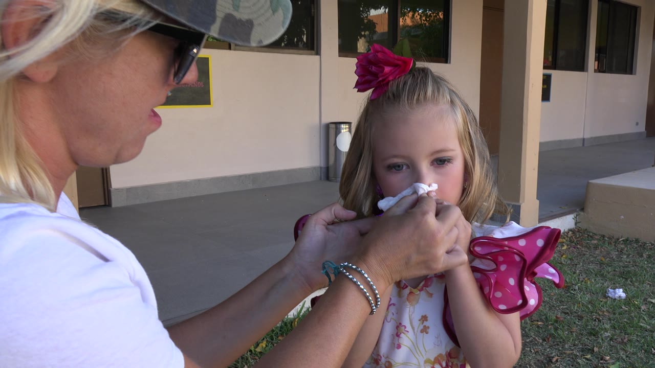 In Cabo San Lucas, Mexico, the woman keeps a tissue pressed to the young girl's nose while the child looks forward beside a shaded walkway.