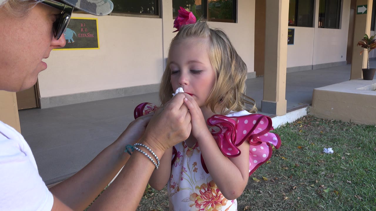 Girl faces forward while a woman wipes near her mouth.