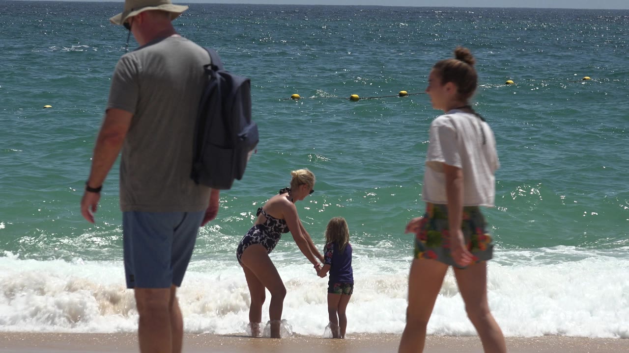Woman and child holding hands at the edge of ocean waves.