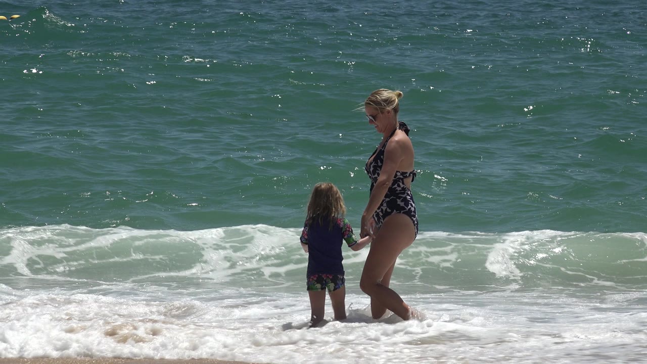 Woman and child holding hands in shallow surf