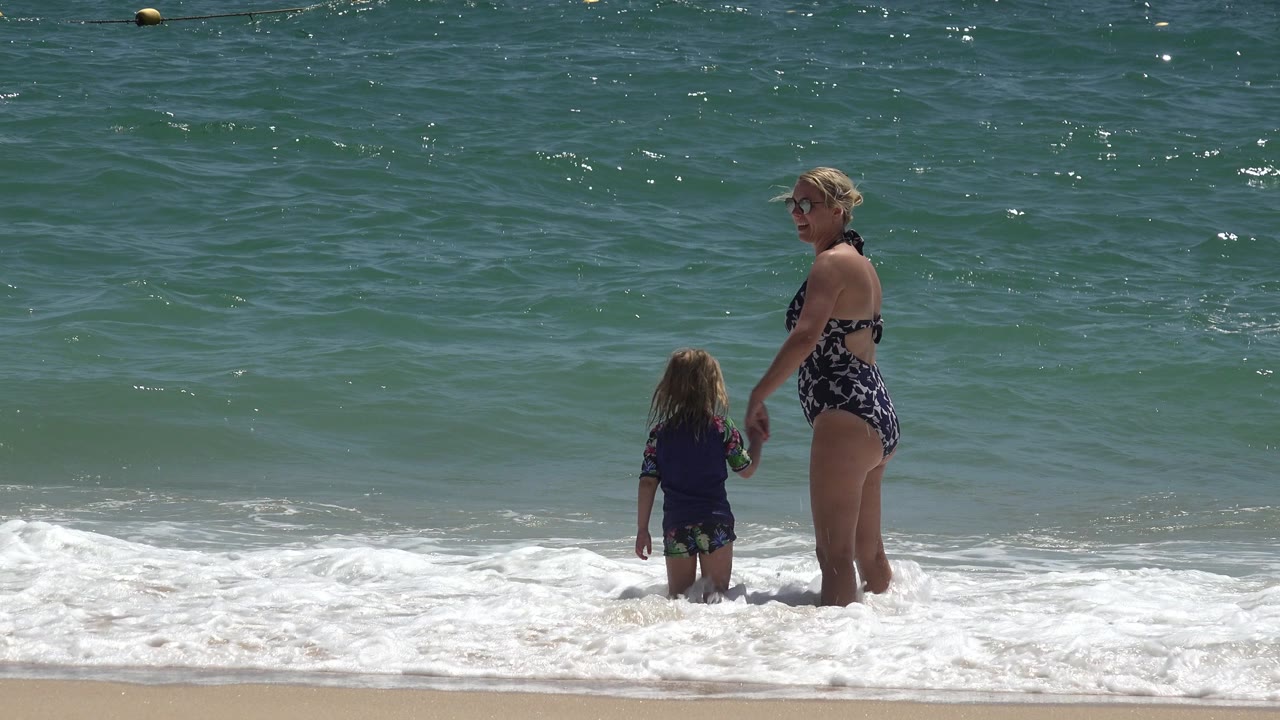 Woman and child standing in shallow surf with open water behind them.