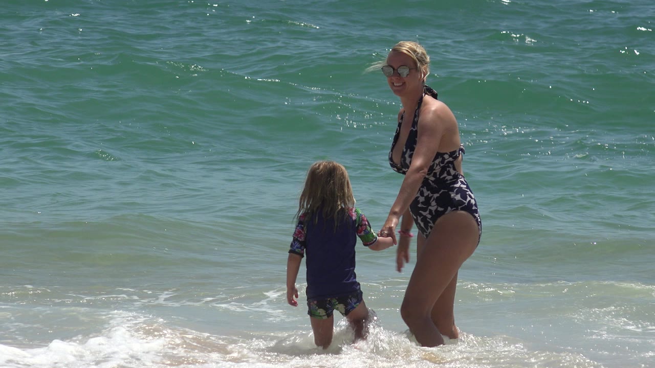 Blonde woman and young girl holding hands in shallow surf.