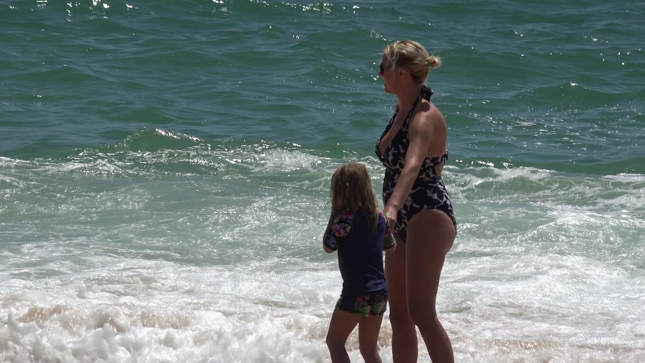 Woman and young child standing at the edge of ocean surf.