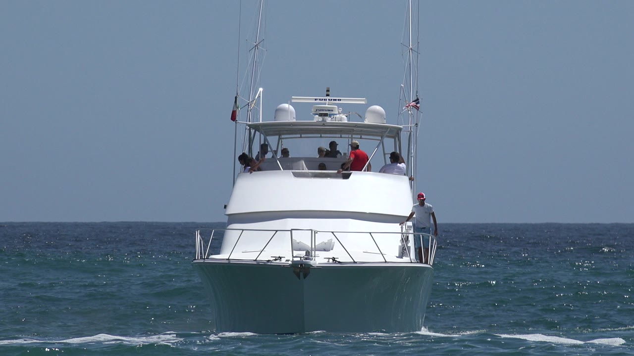 White yacht approaching on blue ocean water with passengers visible.