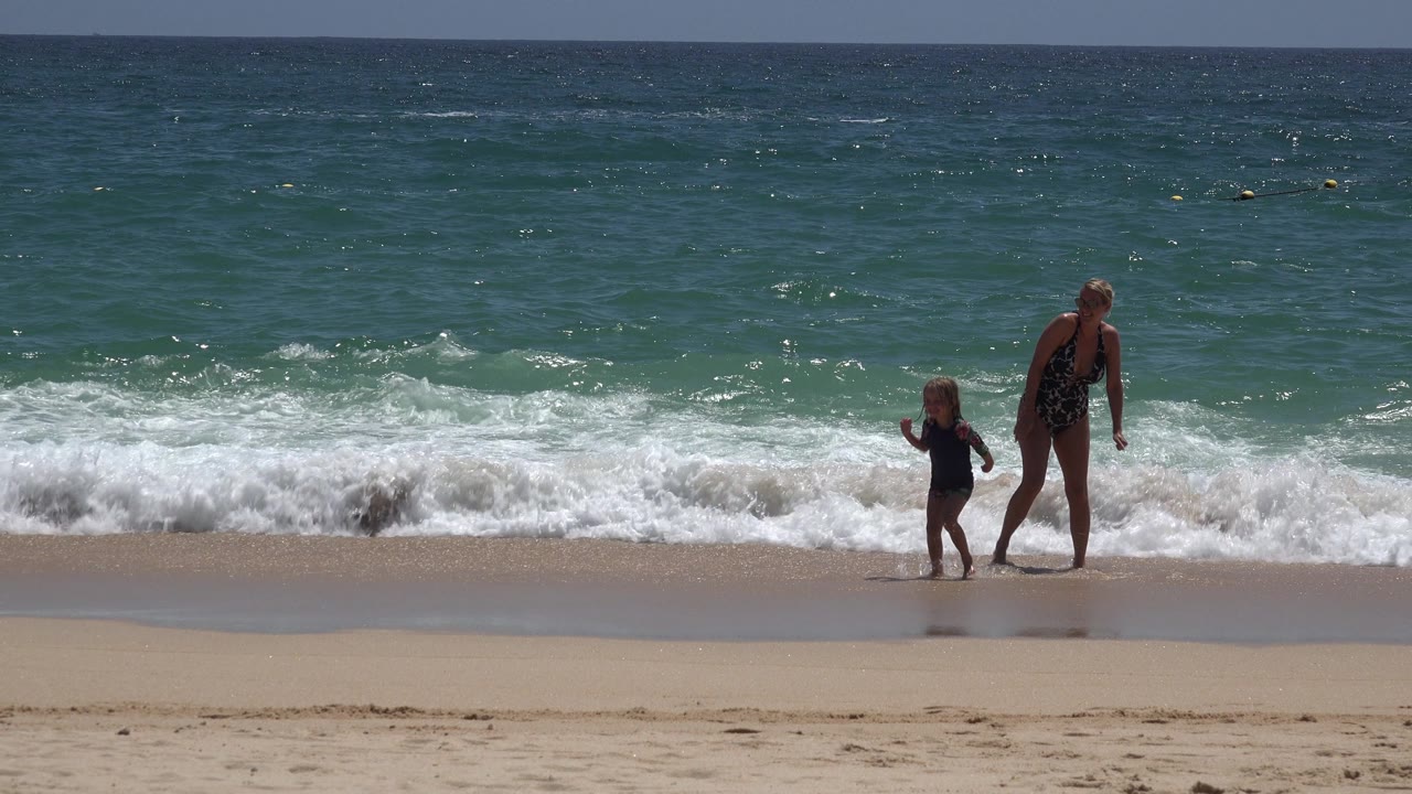 Woman and child moving along the waterline with waves behind them.