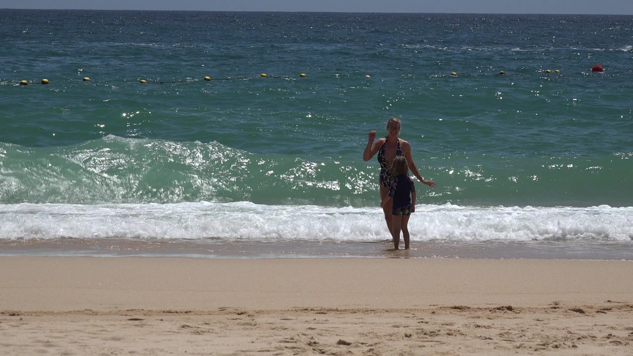 Woman stands near the surf on a sunny beach.