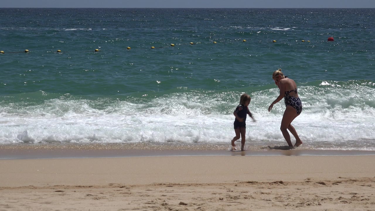 Woman and child at the edge of beach waves