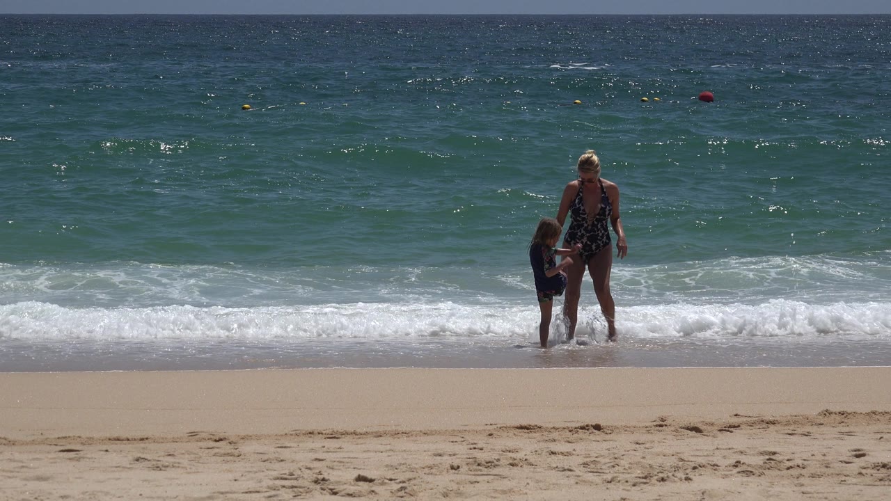 Woman and child stand farther right in the surf with open ocean behind them.