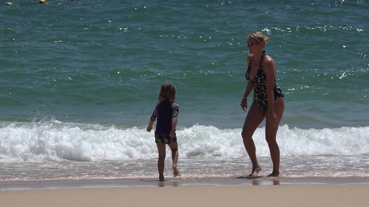 Mother and child standing at the edge of foamy surf.