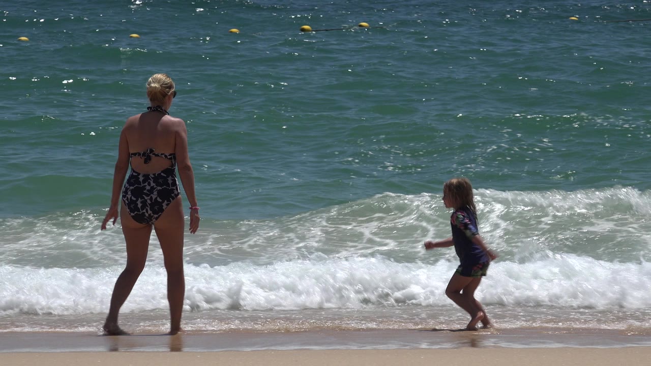 Woman and child at the edge of ocean surf.