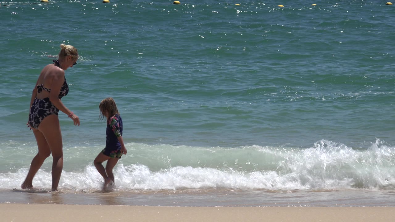 Woman and young child standing in small waves at the beach.