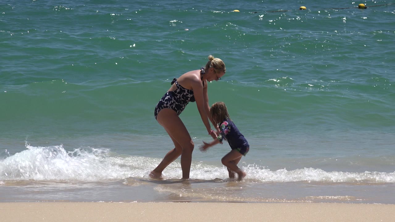 Woman and young child holding hands at the edge of breaking surf.