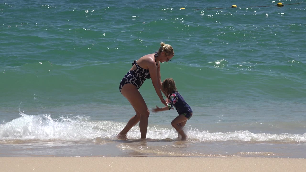 In Cabo San Lucas, Mexico, the woman leans toward the child while white foam curls around their feet and open green-blue water fills the background.