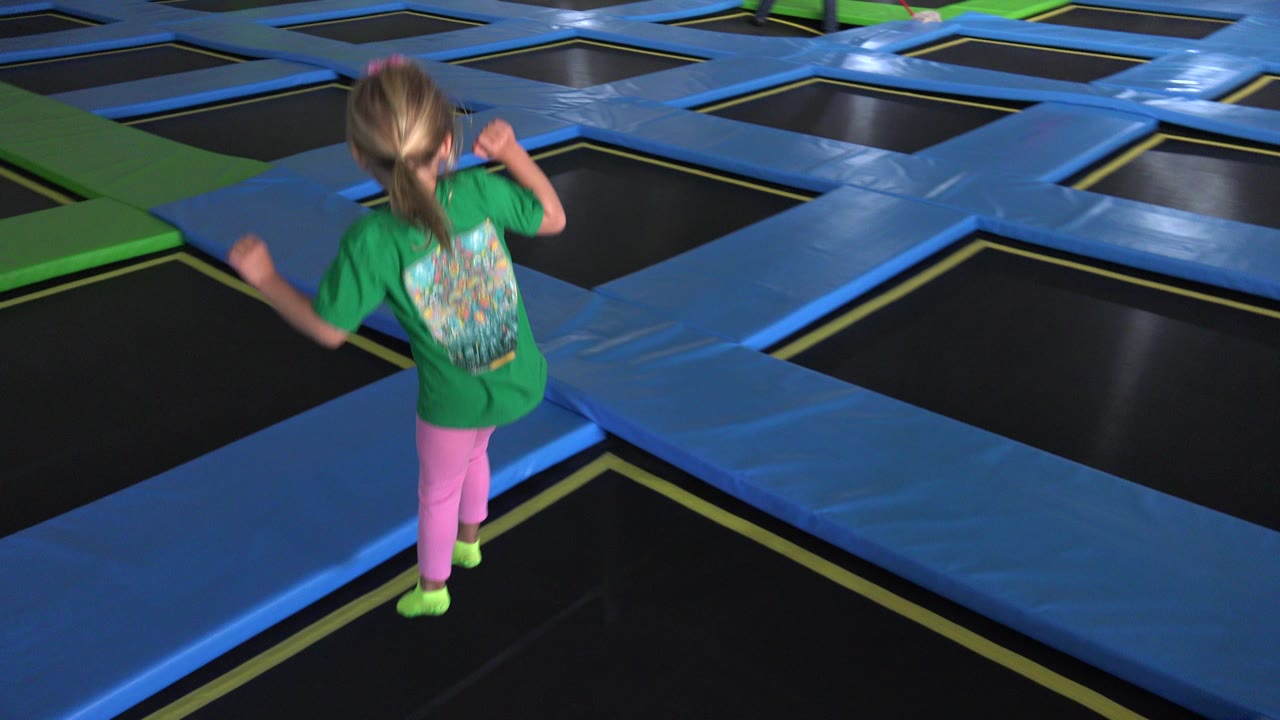 Child in green shirt on an indoor trampoline grid.