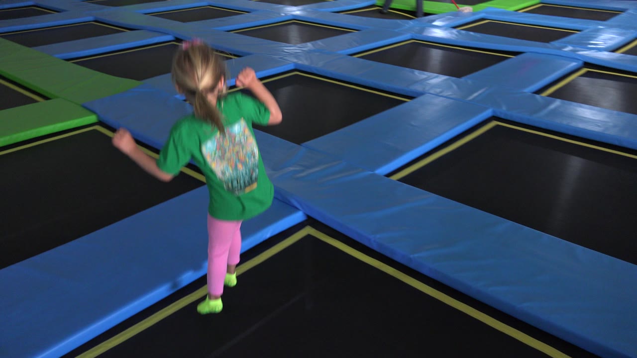The child moves away from the camera across blue padded lanes between black trampoline squares inside the Cabo San Lucas indoor play area.