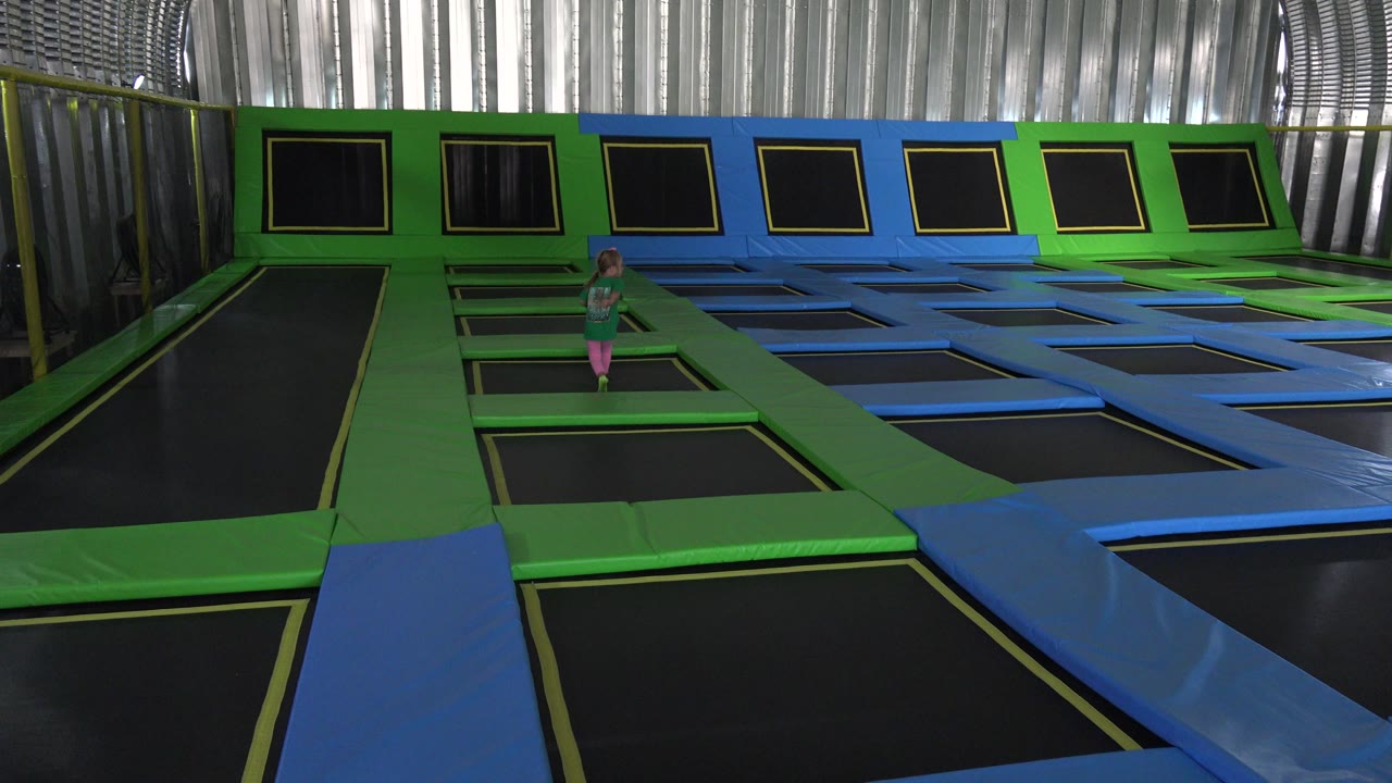 Young girl standing among indoor trampoline mats.