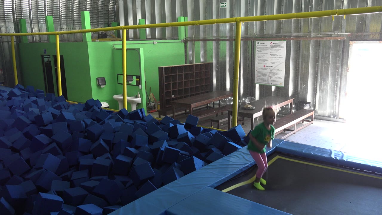 Young girl jumping on an indoor trampoline beside a blue foam pit.