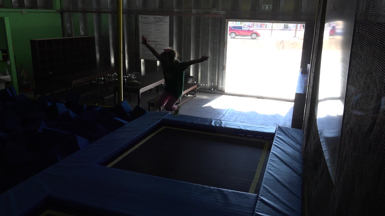 A child in silhouette stands near the edge of an indoor trampoline in Cabo San Lucas, Mexico, with arms raised and bright daylight coming through an open doorway.