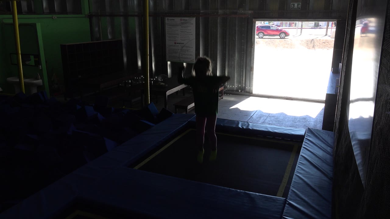 Child jumping or raising arms on trampoline mats near a bright doorway.