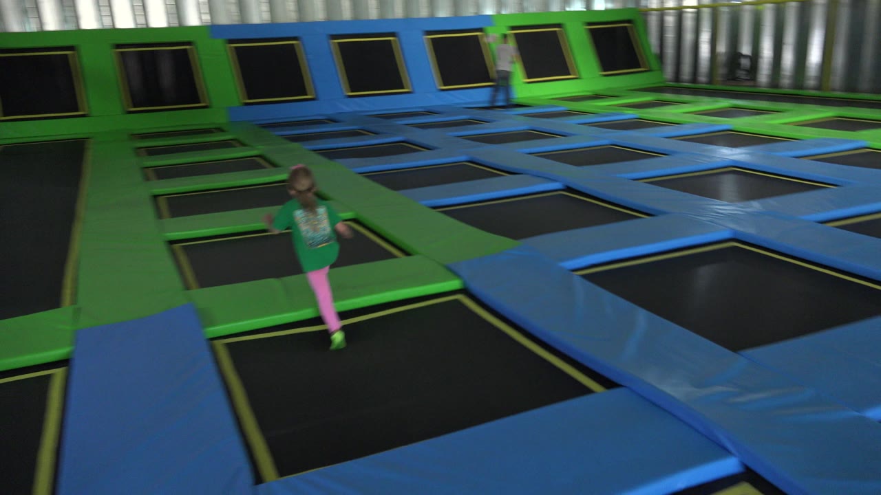 Small girl near foreground trampolines in an indoor play area.