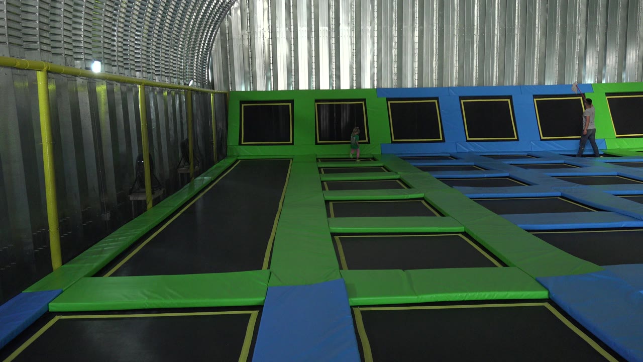 Wide indoor trampoline room with a girl and an adult near the back wall.