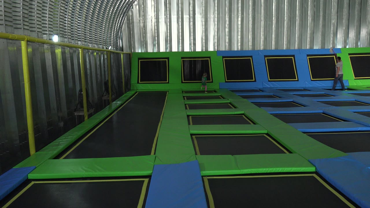 At 0:01 in Cabo San Lucas, Mexico, the girl is positioned on the central green trampoline path while the adult remains near the wall-mounted trampoline panels.