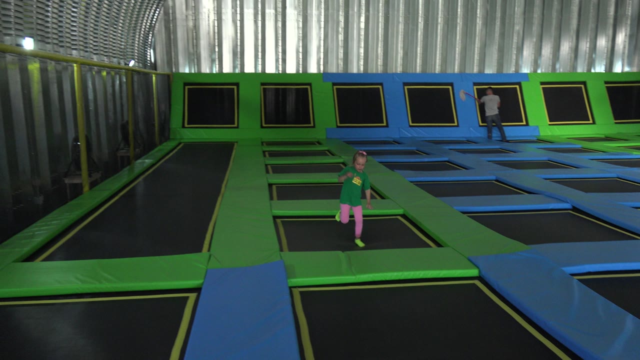 Young girl standing on a green trampoline lane inside an indoor trampoline park.