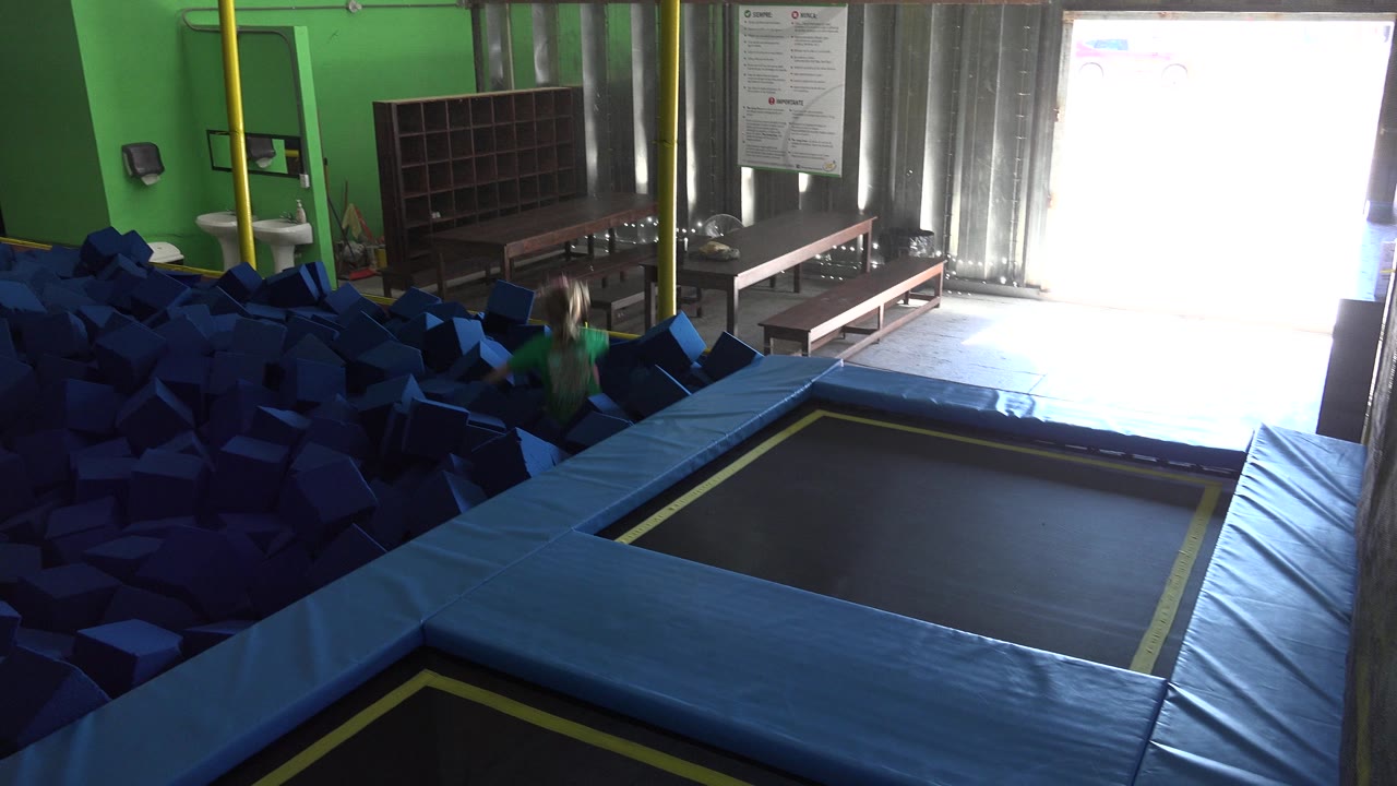 At 0:00 in Cabo San Lucas, Mexico, a child in a green shirt is partly visible near a dark blue foam pit beside blue trampoline padding and a bright doorway.