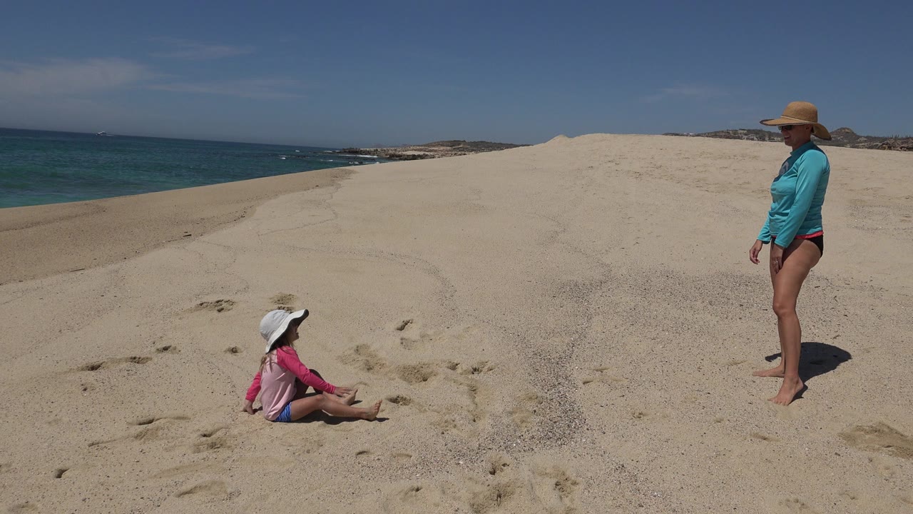 Woman and young girl on sandy beach dunes near the ocean.