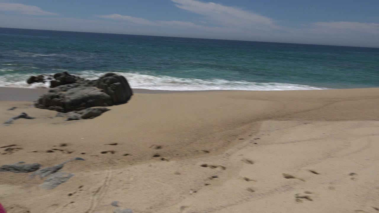 Rocky beach with sand, ocean, surf, and blue sky with no visible people.