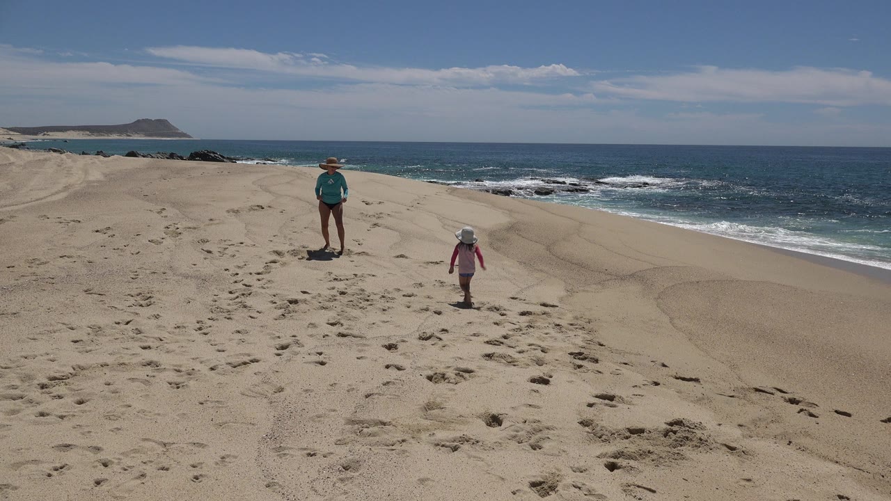 Mother and child standing on a sandy beach above the surf.