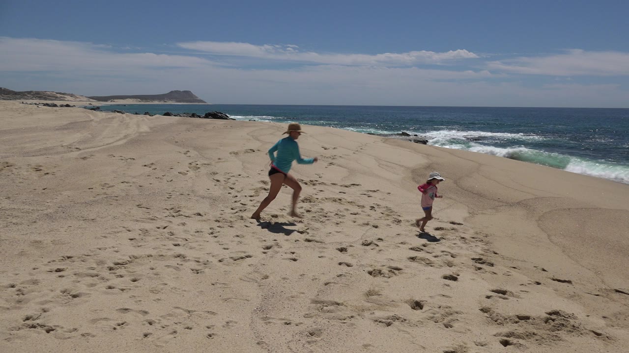Woman and child running on a sandy beach beside the ocean.