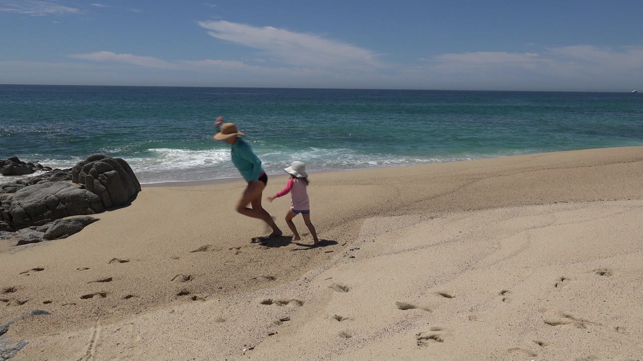 Woman and young girl running on a sandy beach near ocean waves.