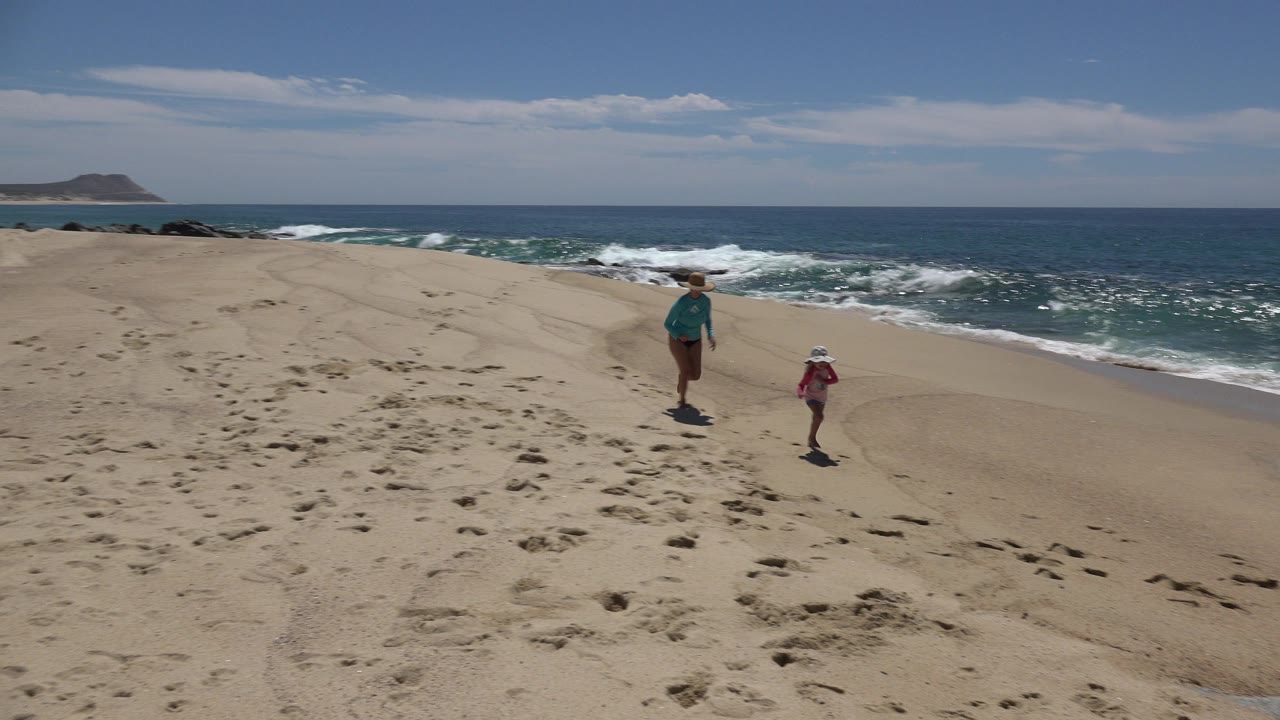 Woman and child on a sandy beach near ocean waves.