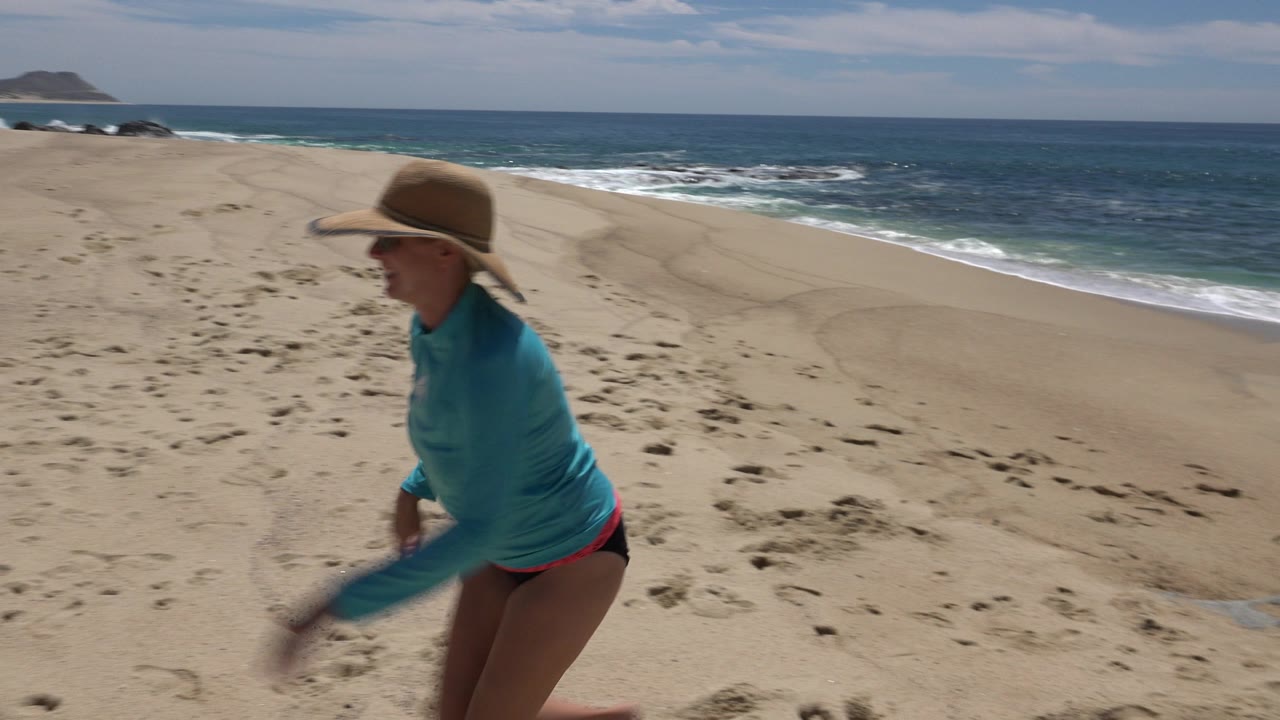 Woman in a hat crossing sandy beach near the ocean.