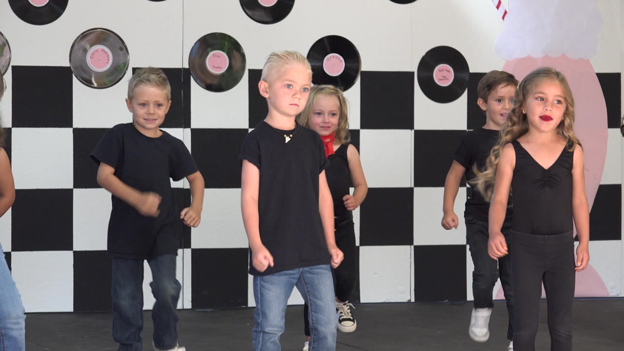 Children perform dance steps on a pink-decorated stage.