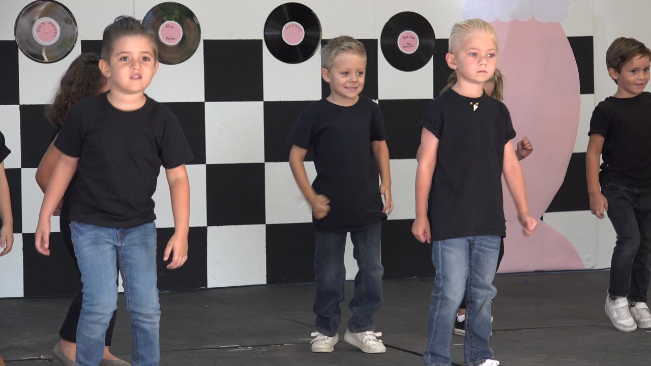 Children in black shirts and jeans dancing on a decorated stage.