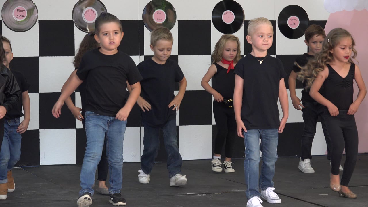 Children continue dance steps with one boy walking across the front.