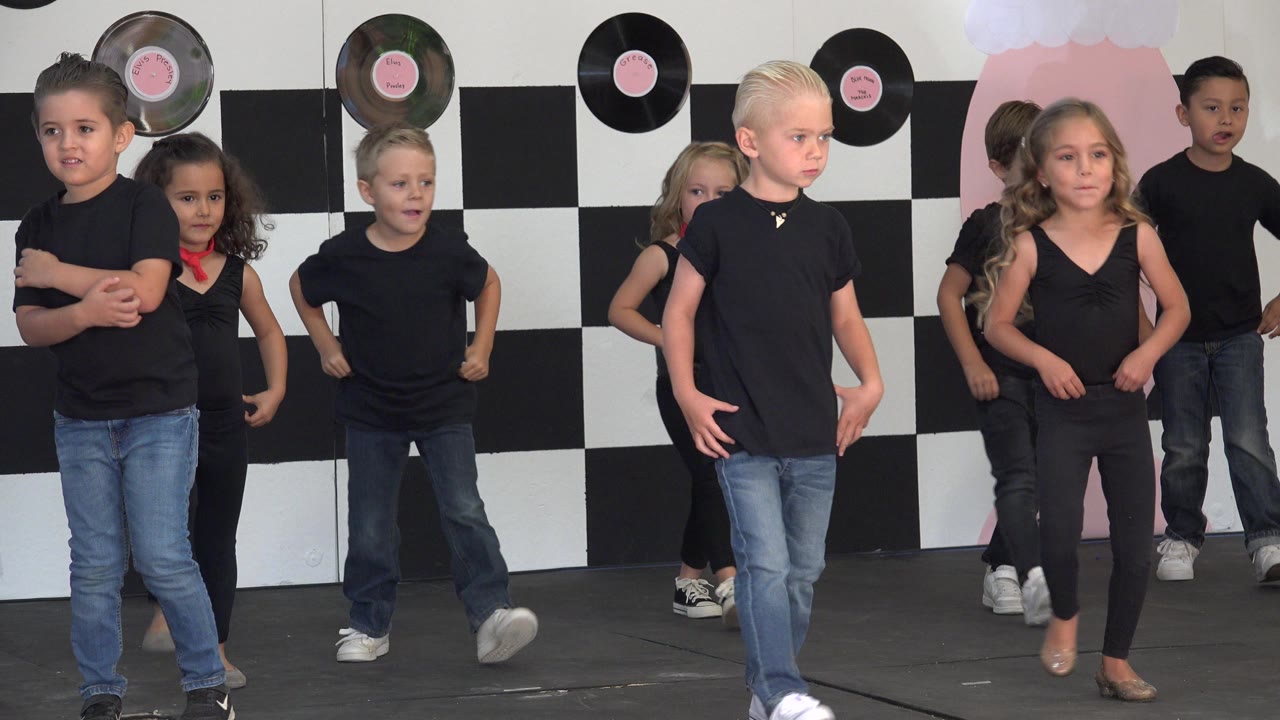 Children in black outfits dancing on a checkerboard stage set.