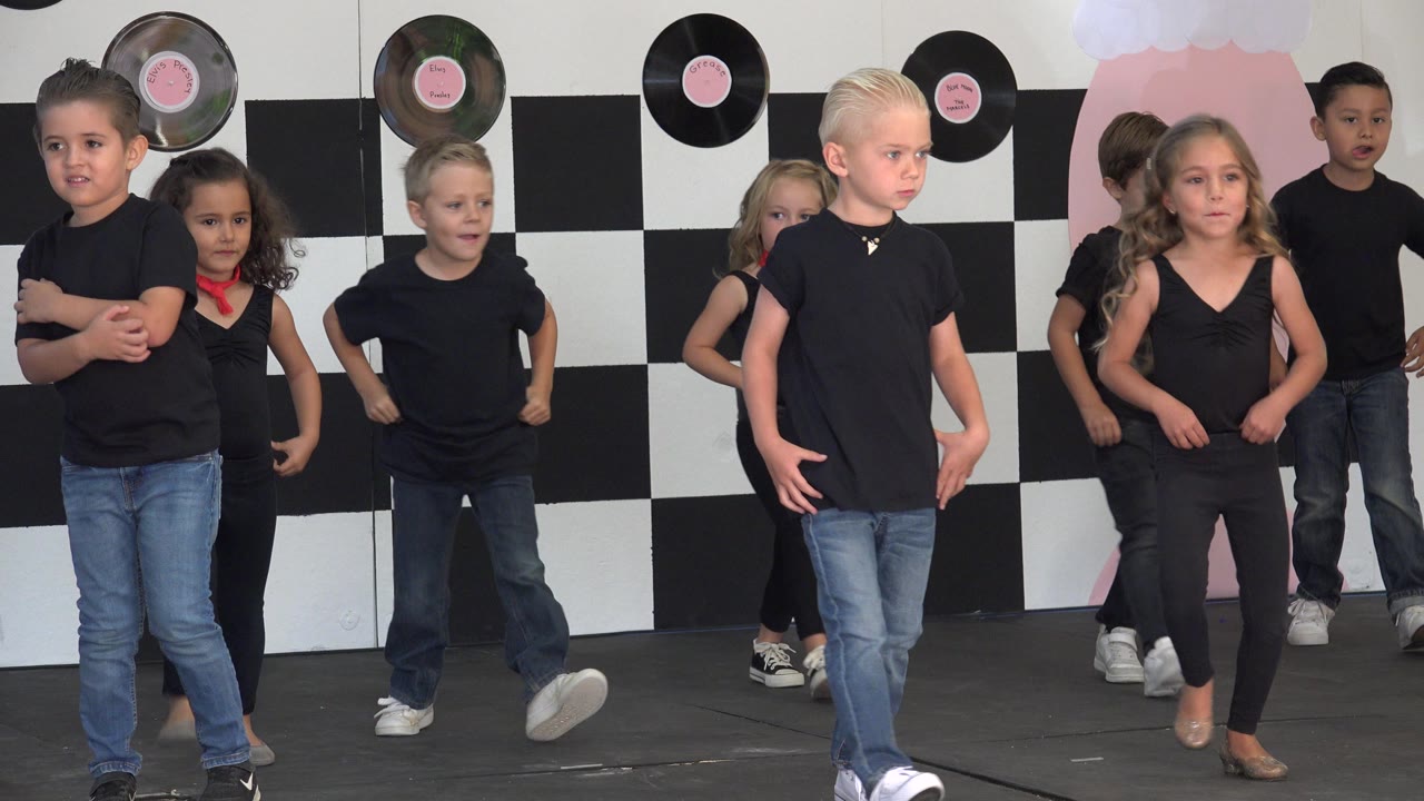 The children continue the routine in Cabo San Lucas, Mexico, with one blond child near the front and other performers spaced across the checkerboard stage set.
