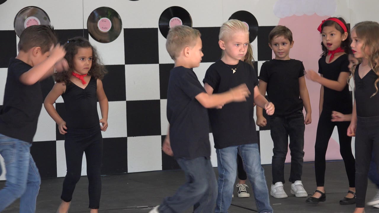 Children in black shirts gather on a decorated stage.
