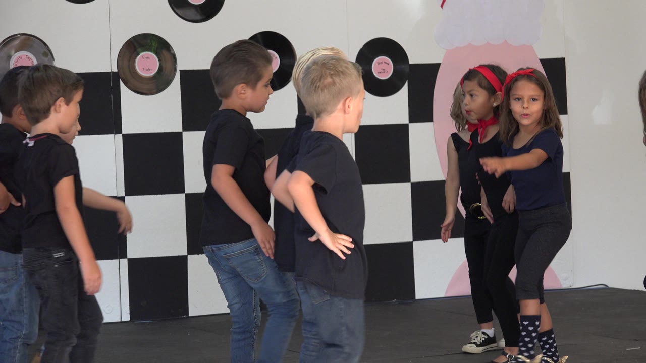 Young boys and girls continue the stage dance in Cabo San Lucas, Mexico, with one girl pointing while boys in black shirts and jeans face her.