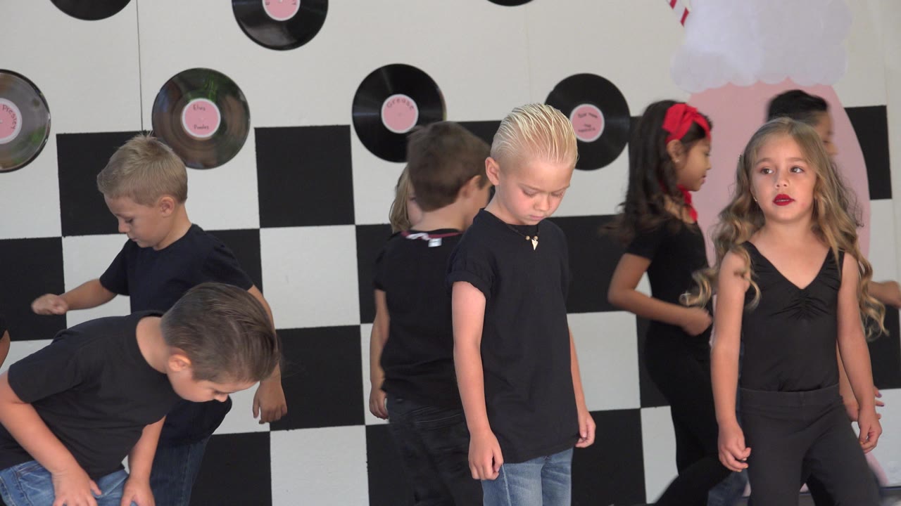 Children in black shirts and jeans move in front of record decorations.