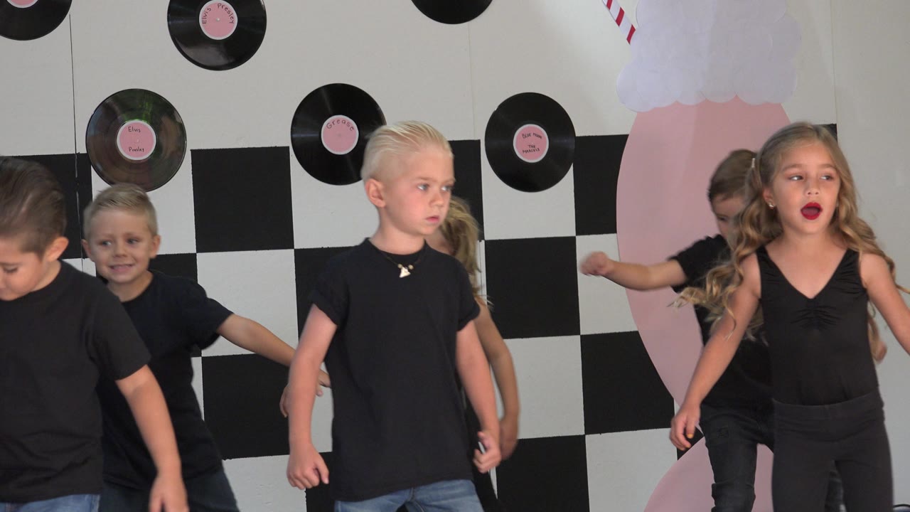 Children in black clothing on a decorated stage backdrop.