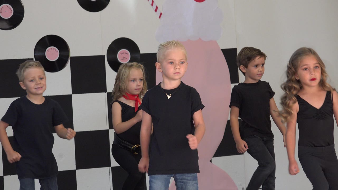 Young children in black dance clothing perform in Cabo San Lucas, Mexico, with vinyl record decorations and a black-and-white checkerboard wall behind them.