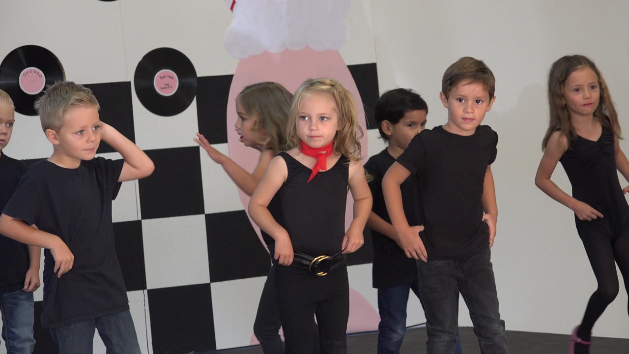 At 0:01 in Cabo San Lucas, Mexico, a blonde child with a red scarf stands near center while other children in black outfits shift positions on the stage.