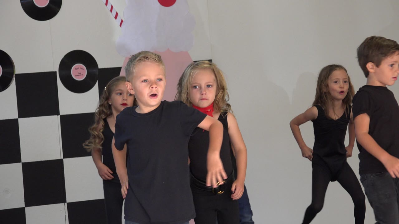 Children in black outfits on a decorated dance recital stage.