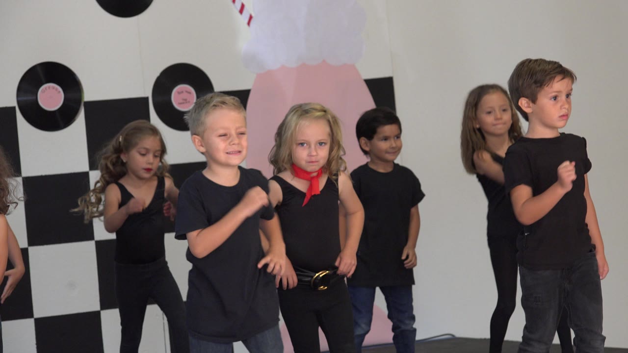 Young boys and girls in black outfits shift their arms and stance during a dance routine against the checkerboard wall in Cabo San Lucas, Mexico.