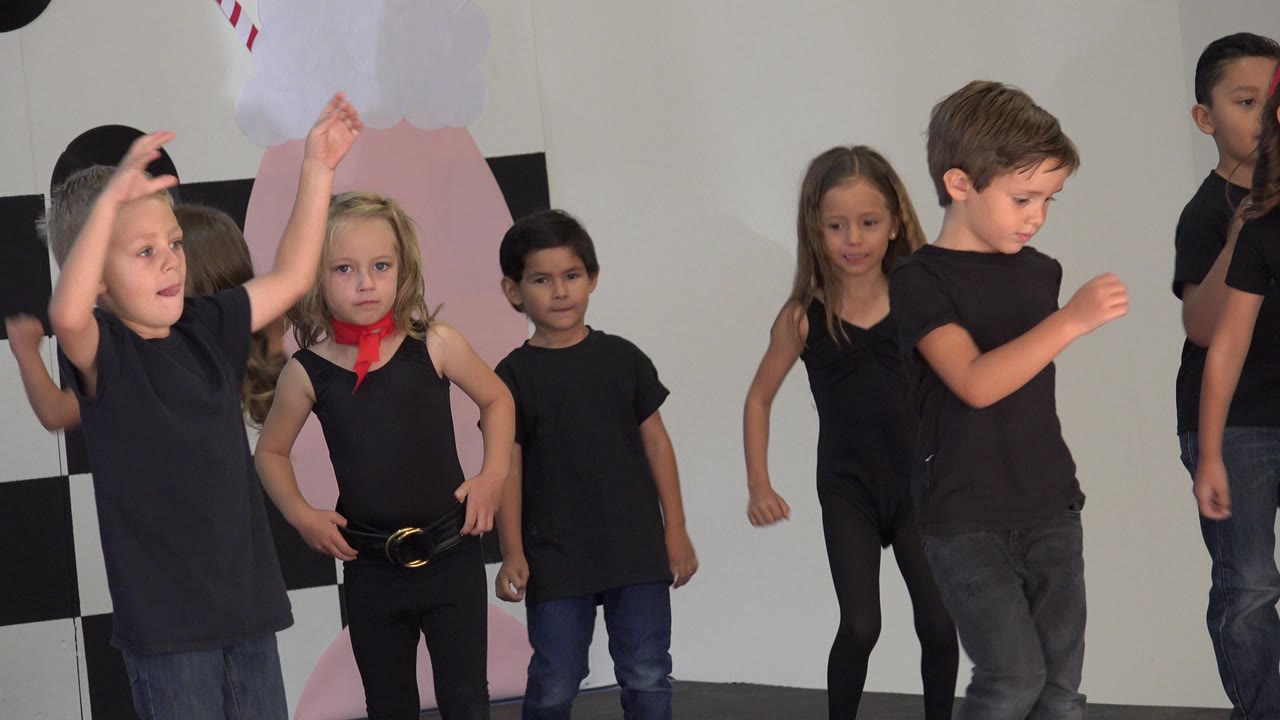 Children in black outfits dancing on an indoor stage.